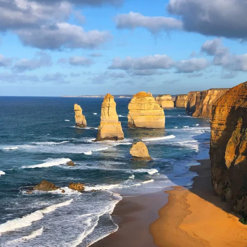 A cyclist enjoying the autumn view of the Twelve Apostles in Australia. The limestone stacks stand tall against the backdrop of a clear blue sky and the crashing ocean waves.